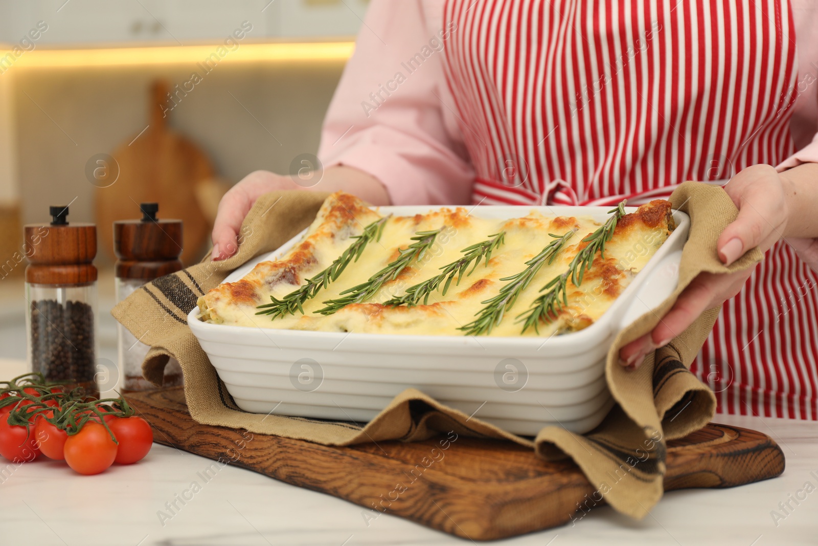 Photo of Woman putting baking dish with tasty lasagna onto white table indoors, closeup