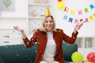 Photo of Happy woman with party popper and confetti in festive decorated room