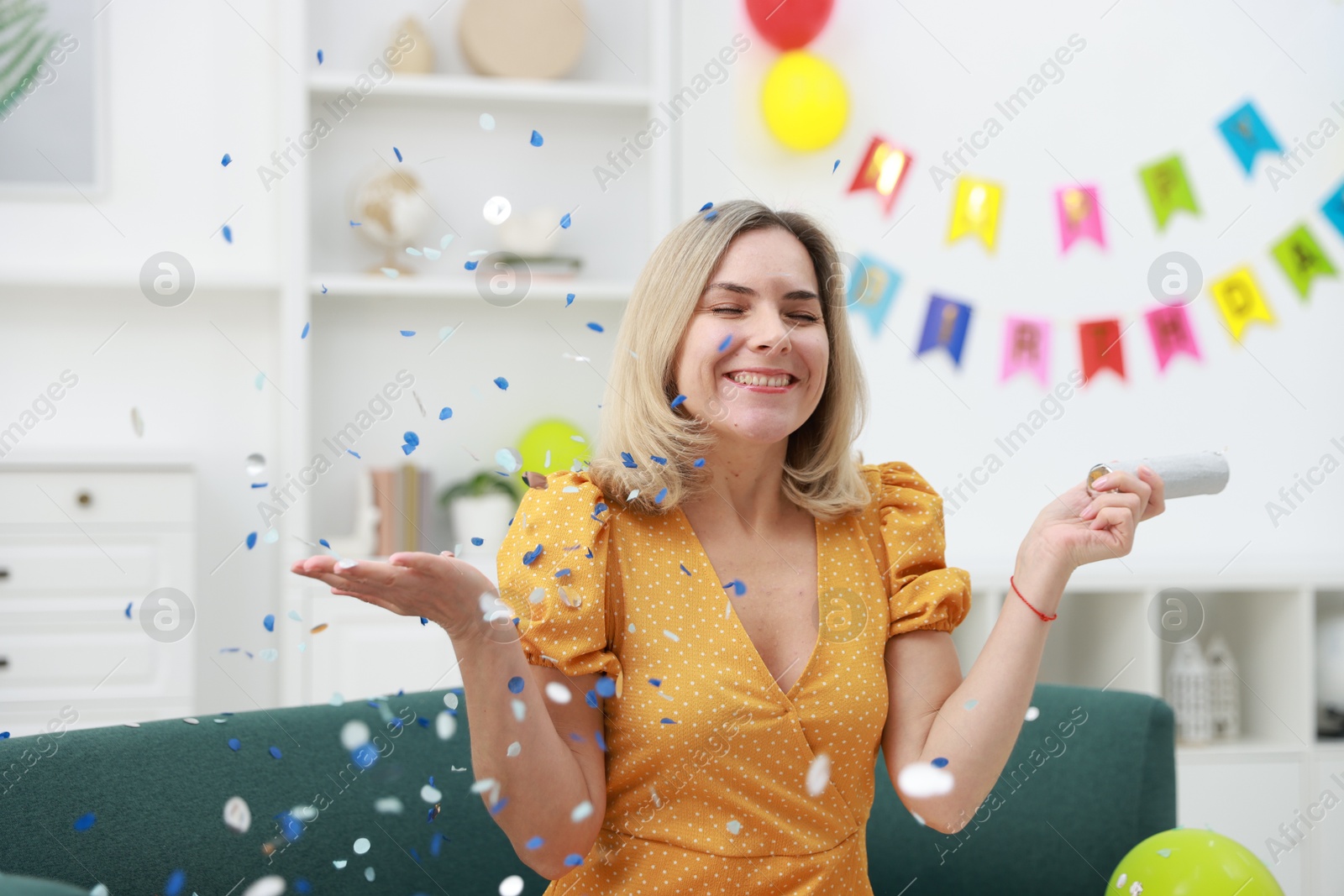 Photo of Happy woman with confetti popper on sofa in room decorated for party