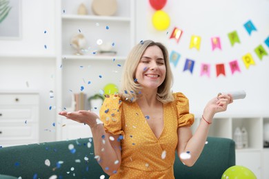 Photo of Happy woman with confetti popper on sofa in room decorated for party