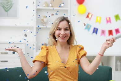 Photo of Happy woman with confetti popper on sofa in room decorated for party