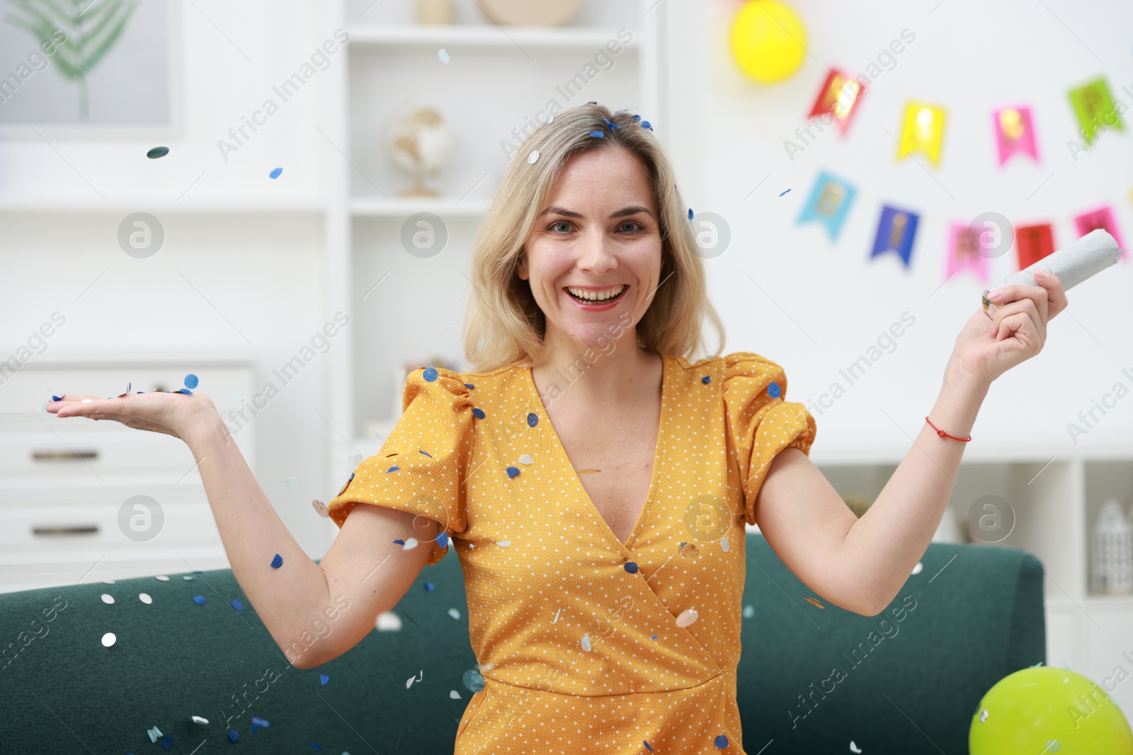 Photo of Happy woman with confetti popper on sofa in room decorated for party