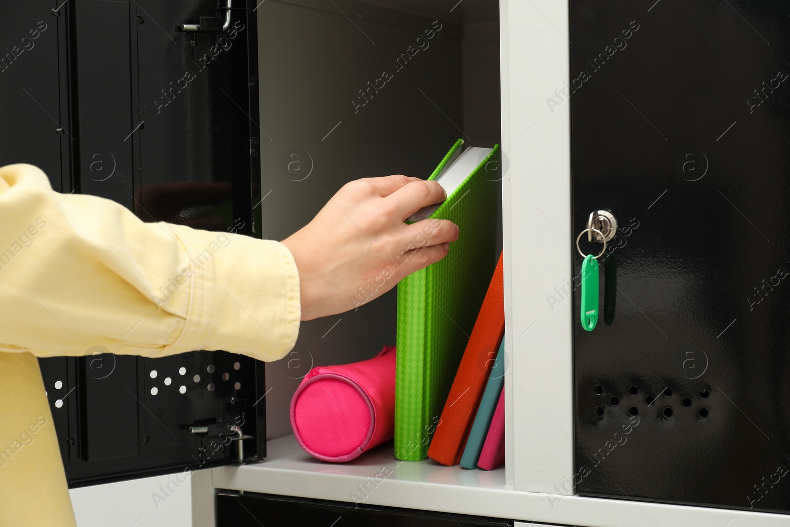 Photo of Woman putting book into locker indoors, closeup