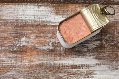 Photo of Tasty canned meat in tin can on wooden table, top view. Space for text