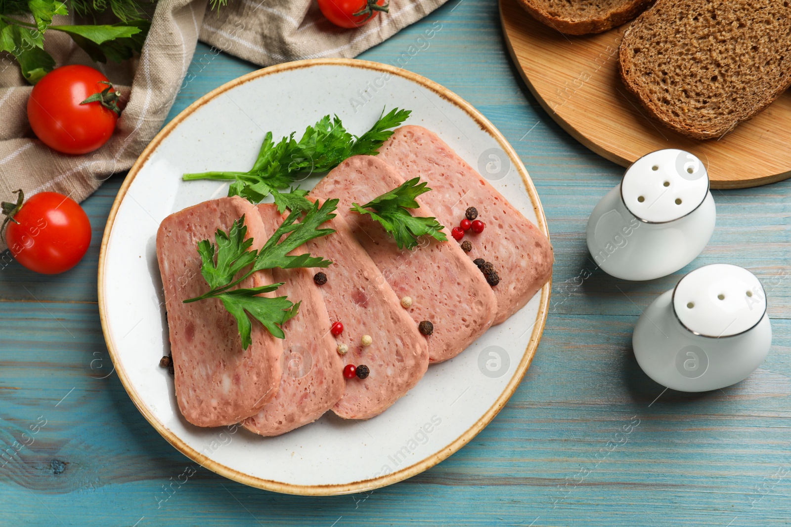 Photo of Tasty canned meat, spices, bread and tomatoes on light blue wooden table, flat lay