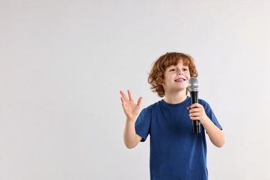 Photo of Little boy with microphone on light grey background, space for text