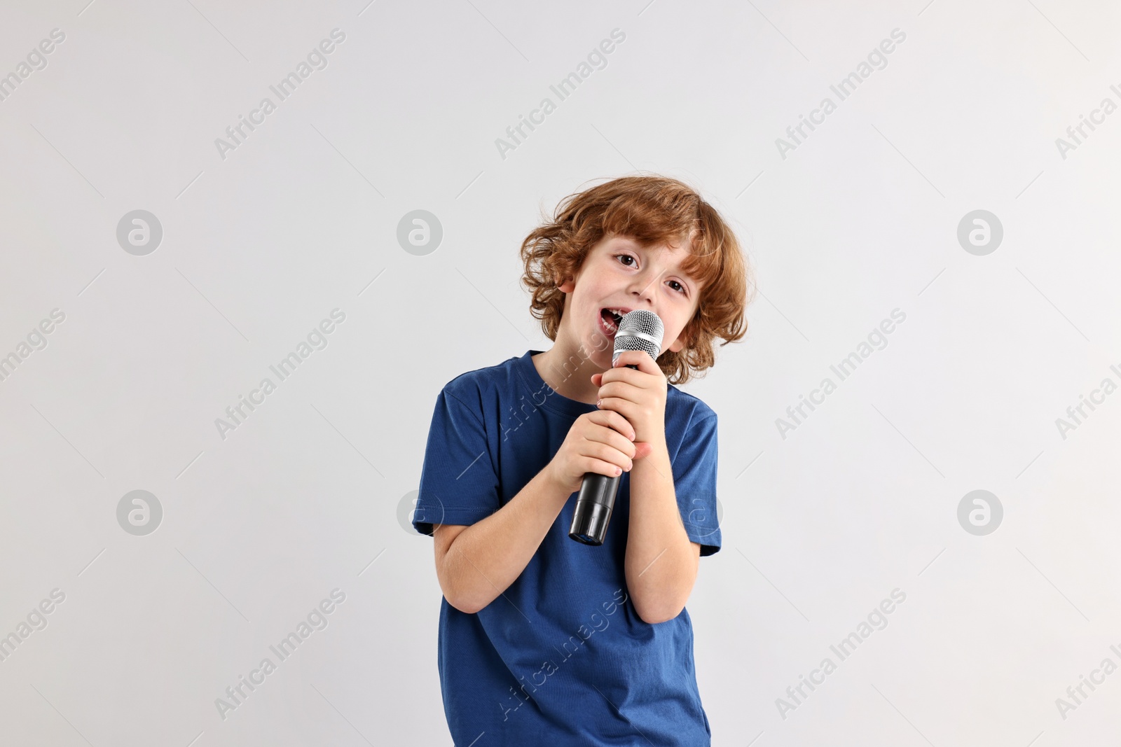 Photo of Little boy with microphone singing on light grey background