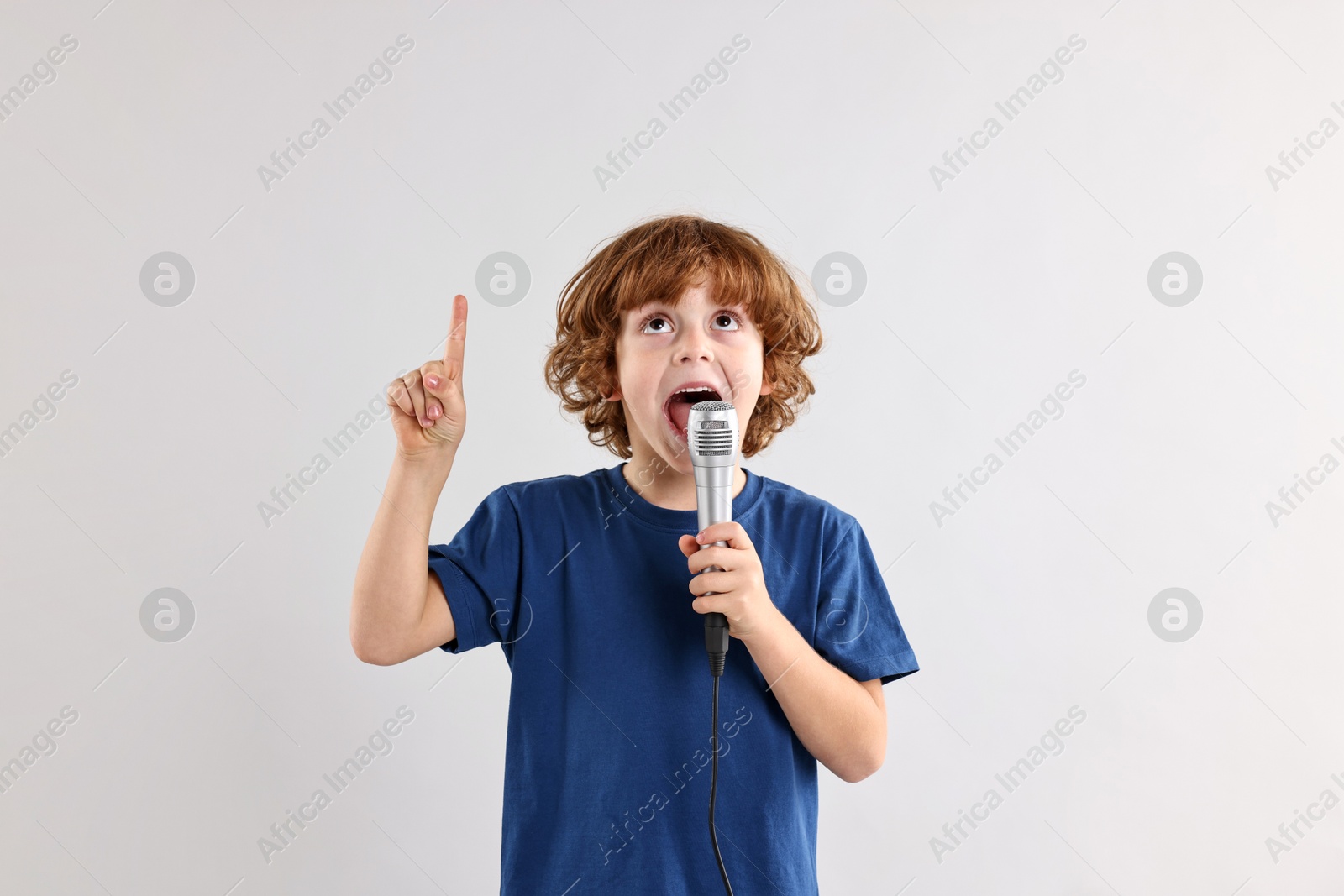 Photo of Little boy with microphone singing on light grey background