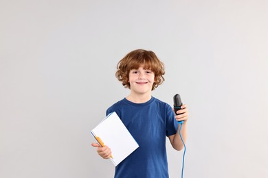 Photo of Little boy with microphone and notebook on light grey background