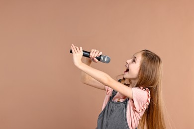 Photo of Little girl with microphone singing on light brown background, space for text