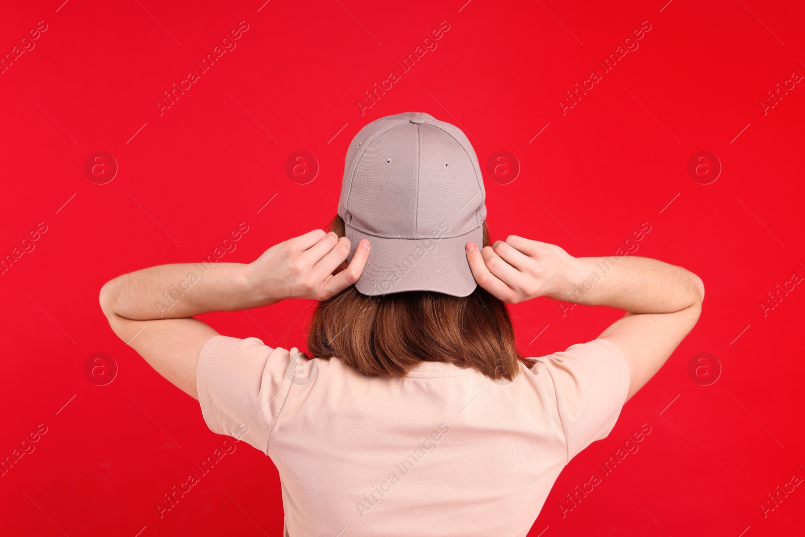 Photo of Woman in stylish baseball cap on red background, back view. Mockup for design