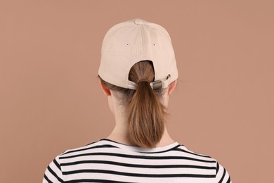 Photo of Woman in stylish baseball cap on beige background, back view. Mockup for design