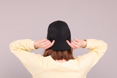 Photo of Woman in stylish baseball cap on grey background, back view. Mockup for design