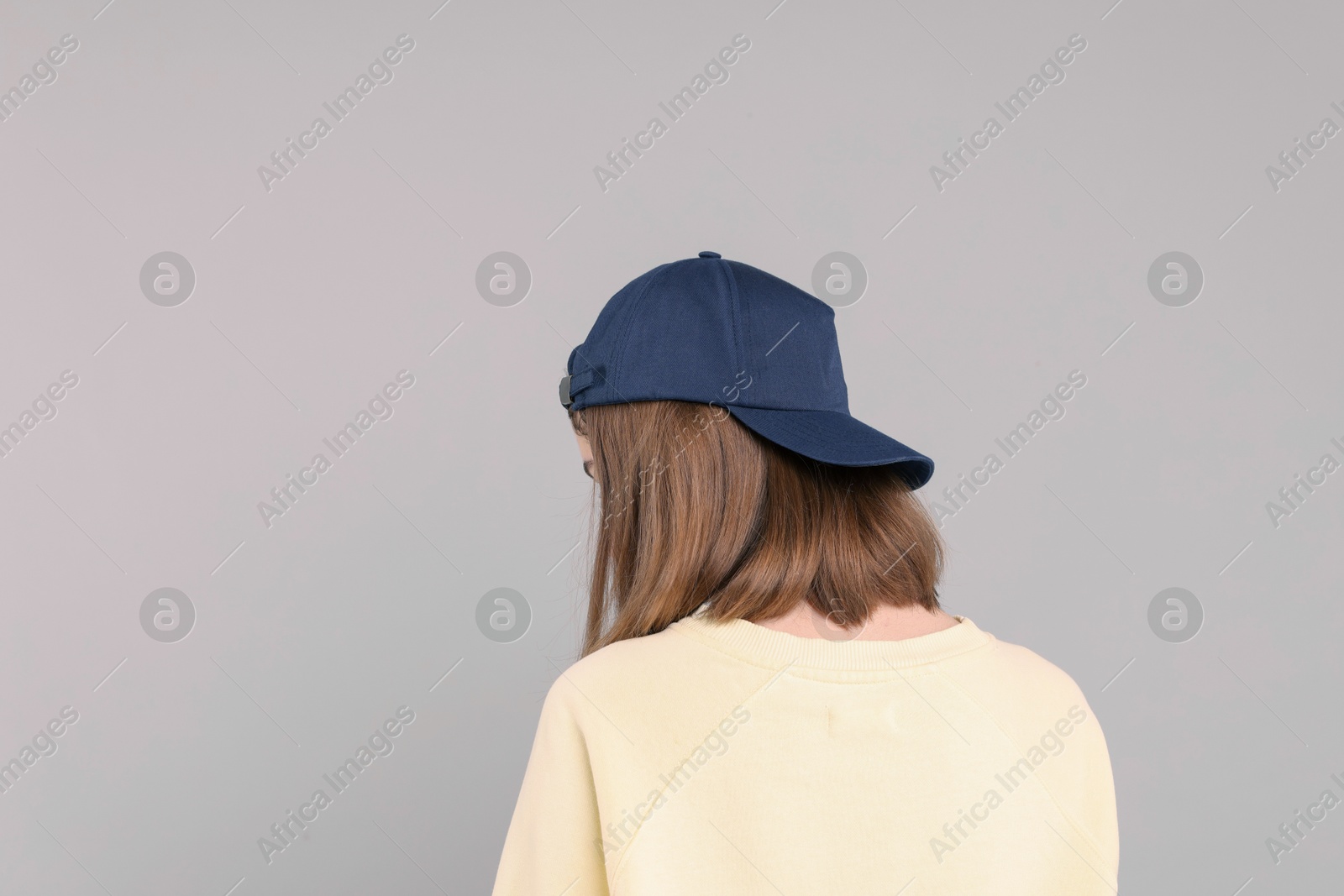 Photo of Woman in stylish baseball cap on grey background, back view. Mockup for design