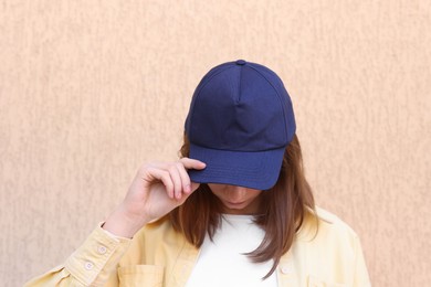 Photo of Woman in stylish baseball cap near beige wall. Mockup for design