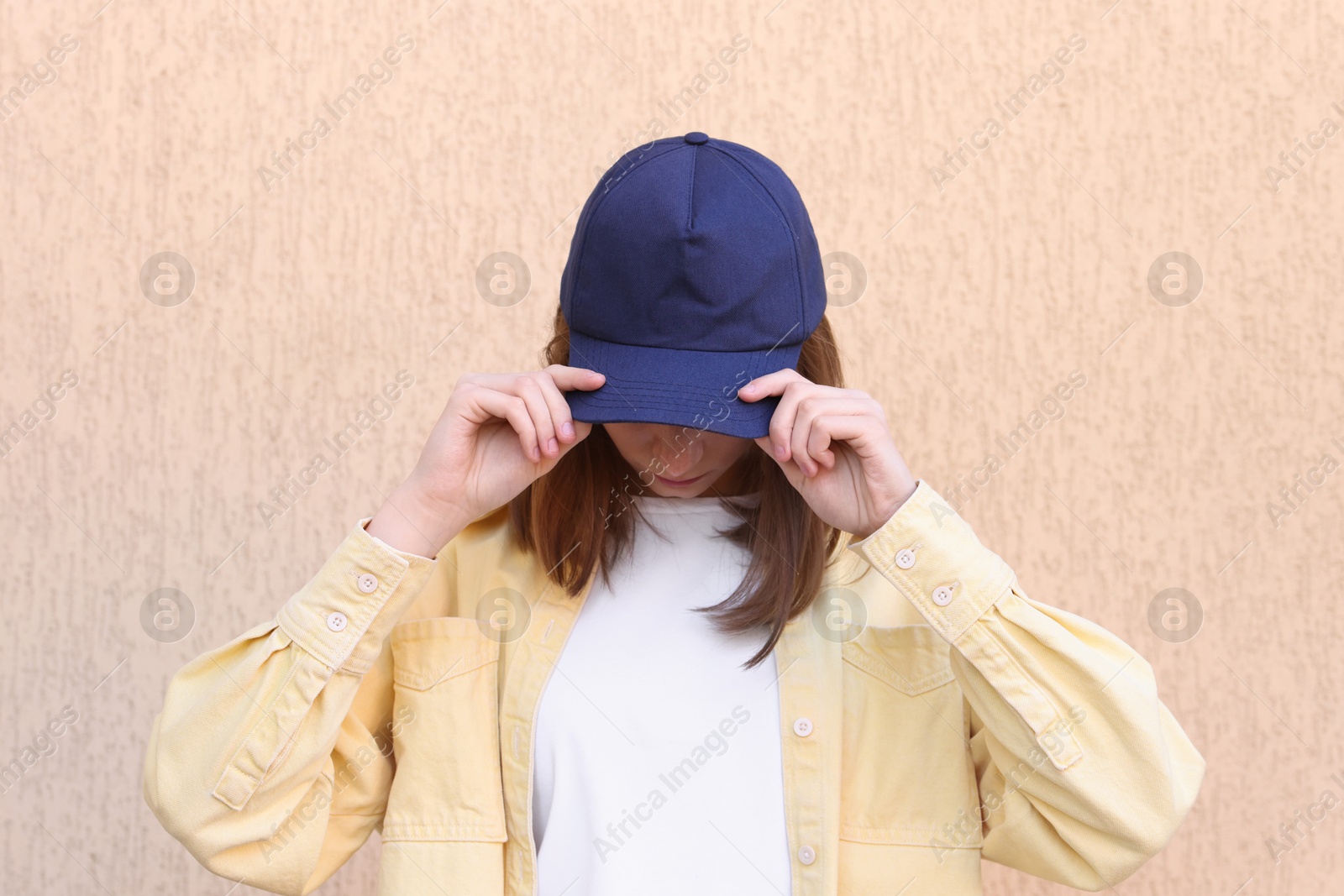 Photo of Woman in stylish baseball cap near beige wall. Mockup for design