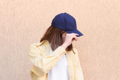 Photo of Woman in stylish baseball cap near beige wall. Mockup for design