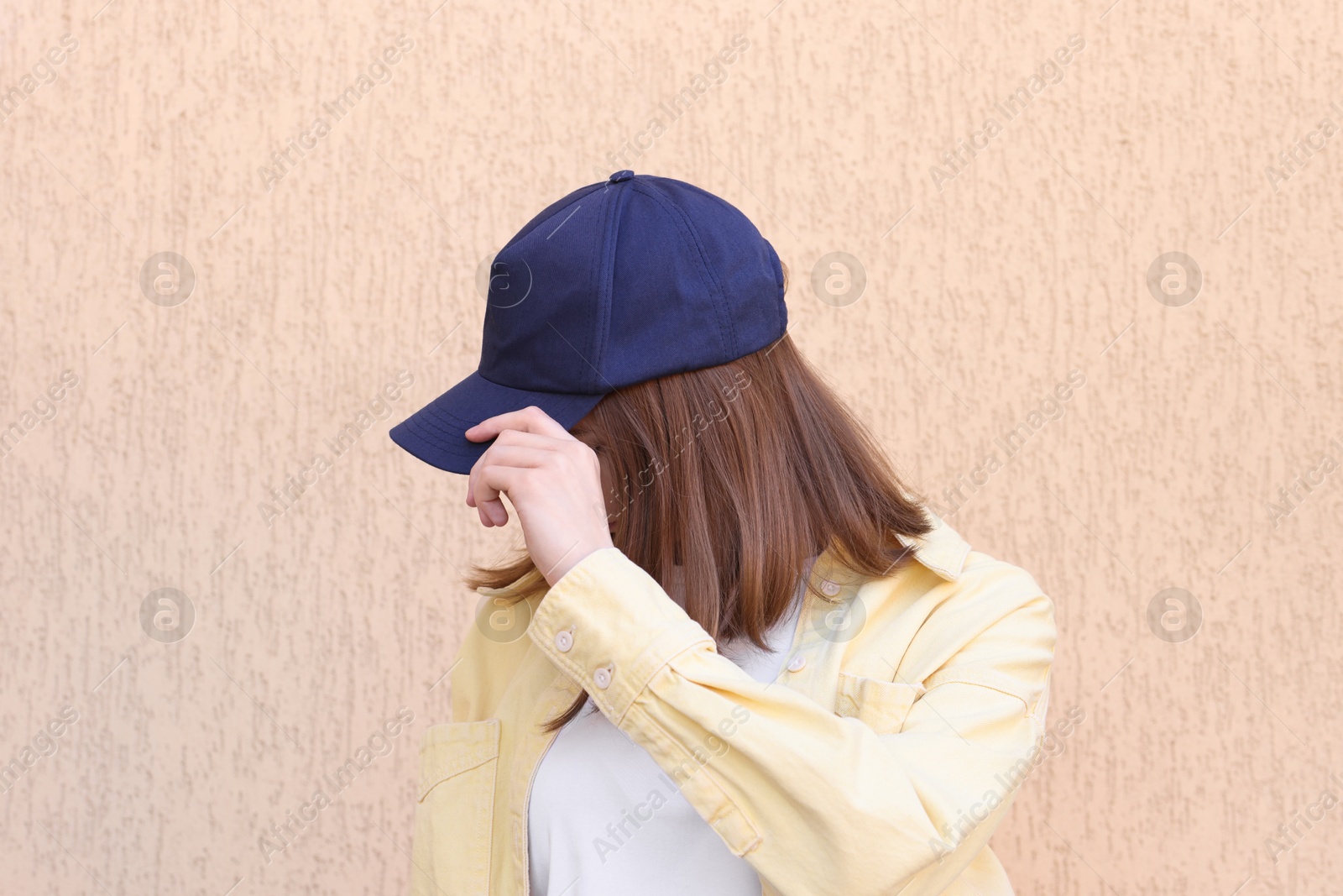 Photo of Woman in stylish baseball cap near beige wall. Mockup for design