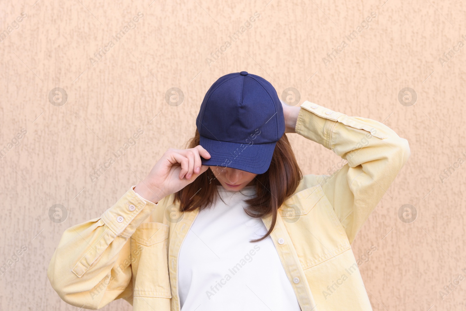 Photo of Woman in stylish baseball cap near beige wall. Mockup for design