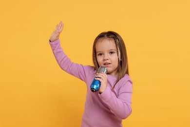 Photo of Cute girl with microphone singing on orange background