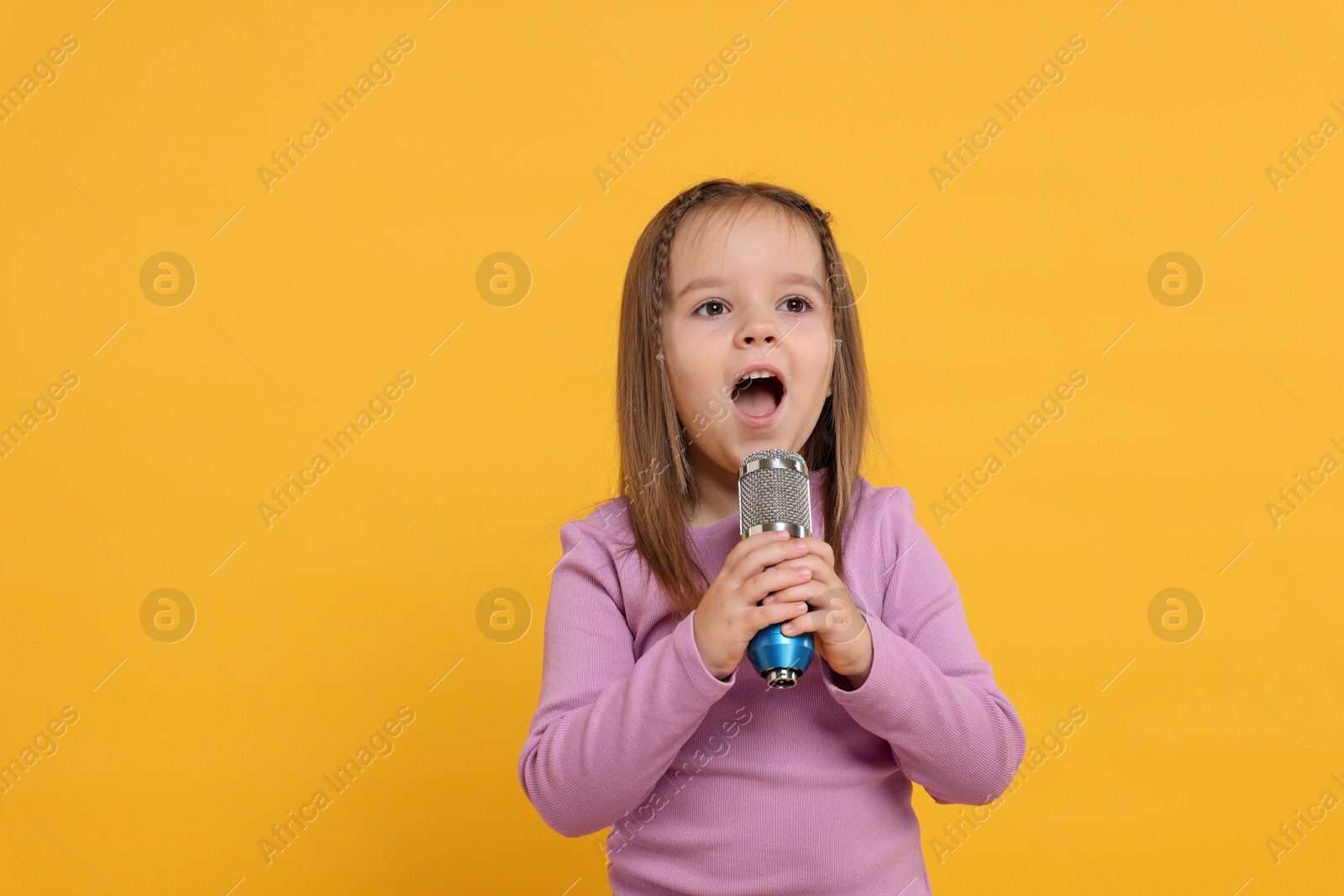 Photo of Cute girl with microphone singing on orange background