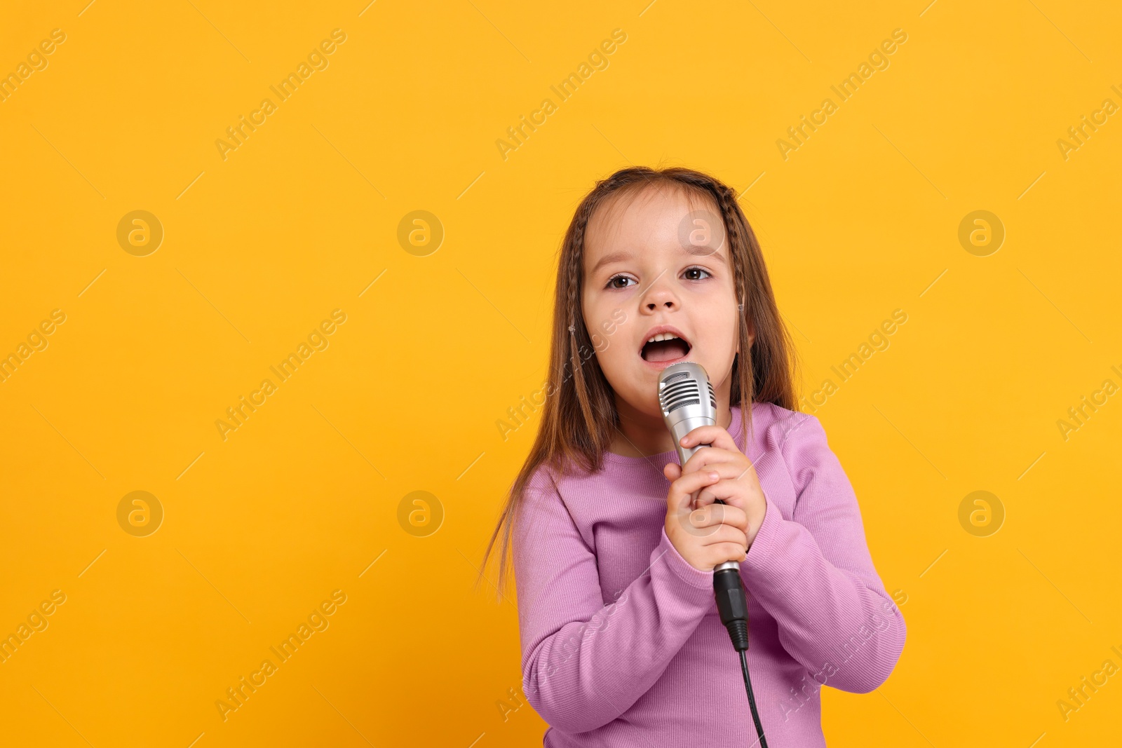 Photo of Cute girl with microphone singing on orange background