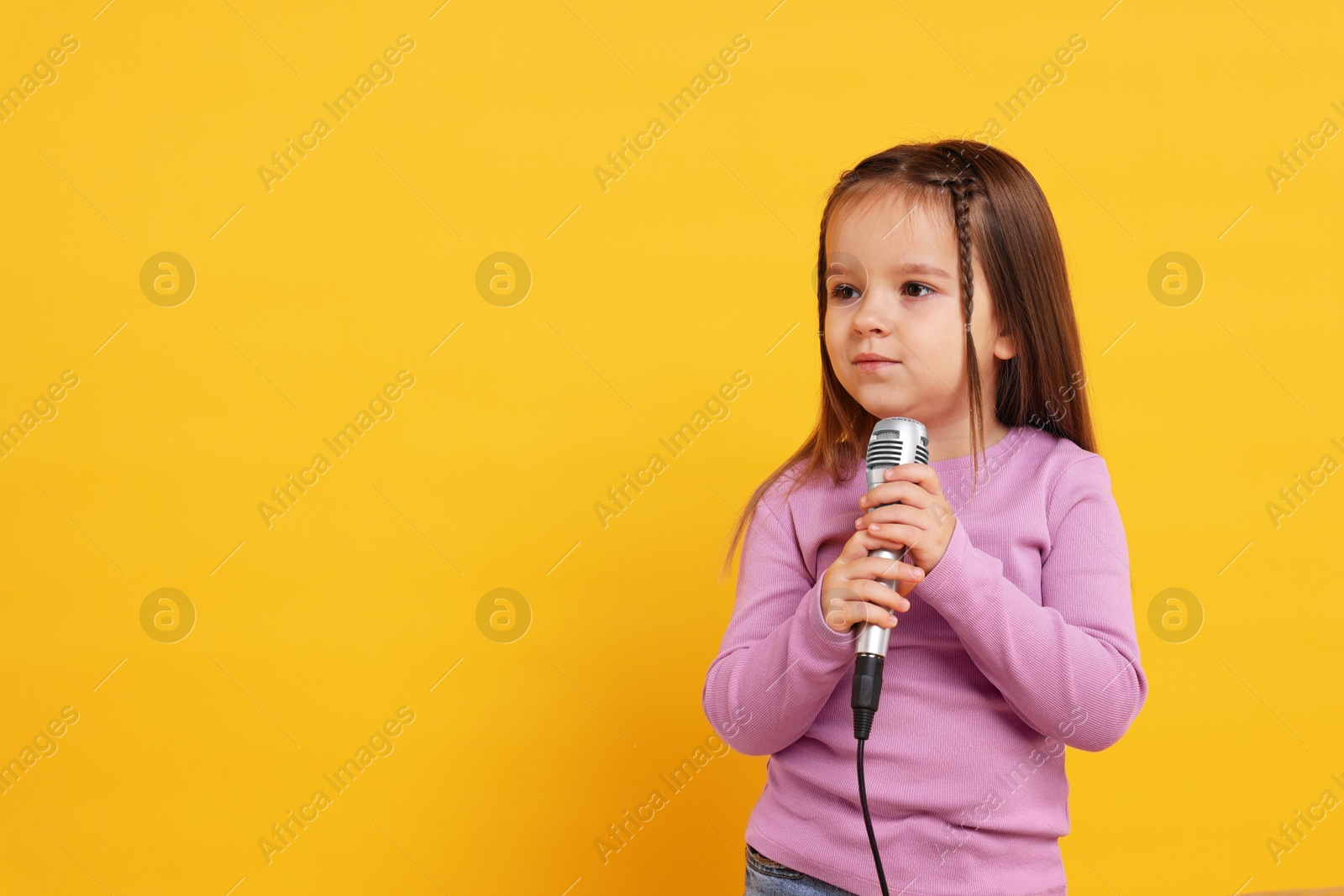 Photo of Cute girl with microphone on orange background. Space for text