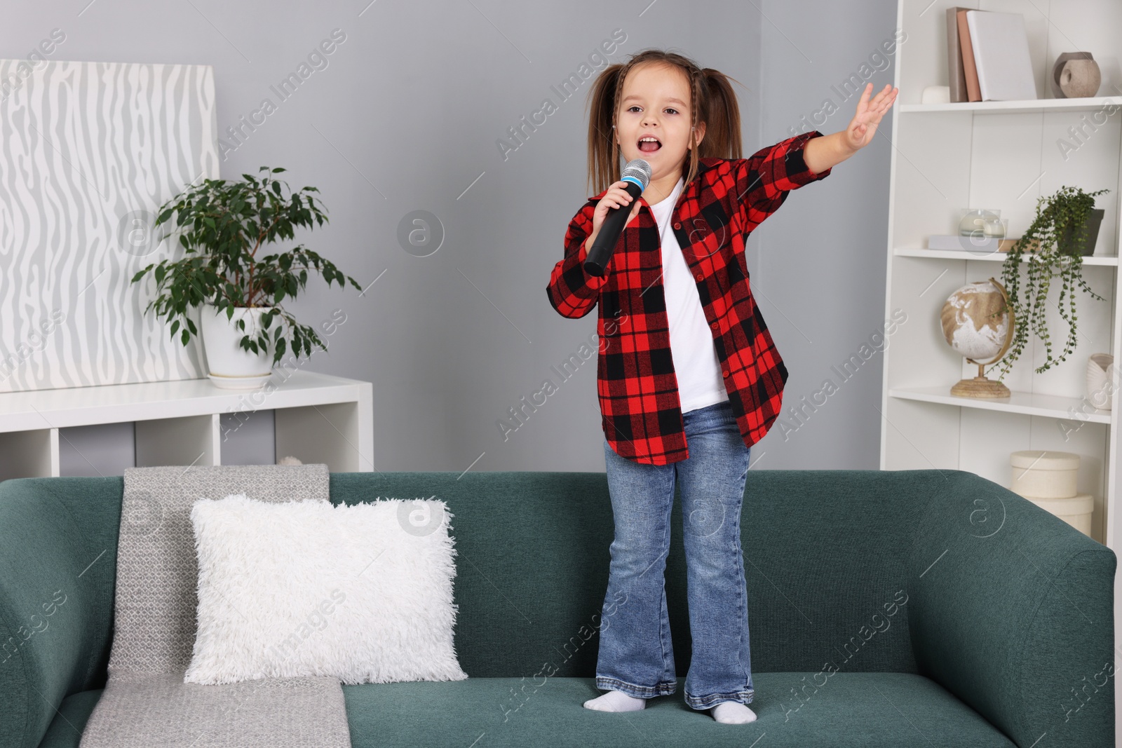 Photo of Cute girl with microphone singing on sofa at home