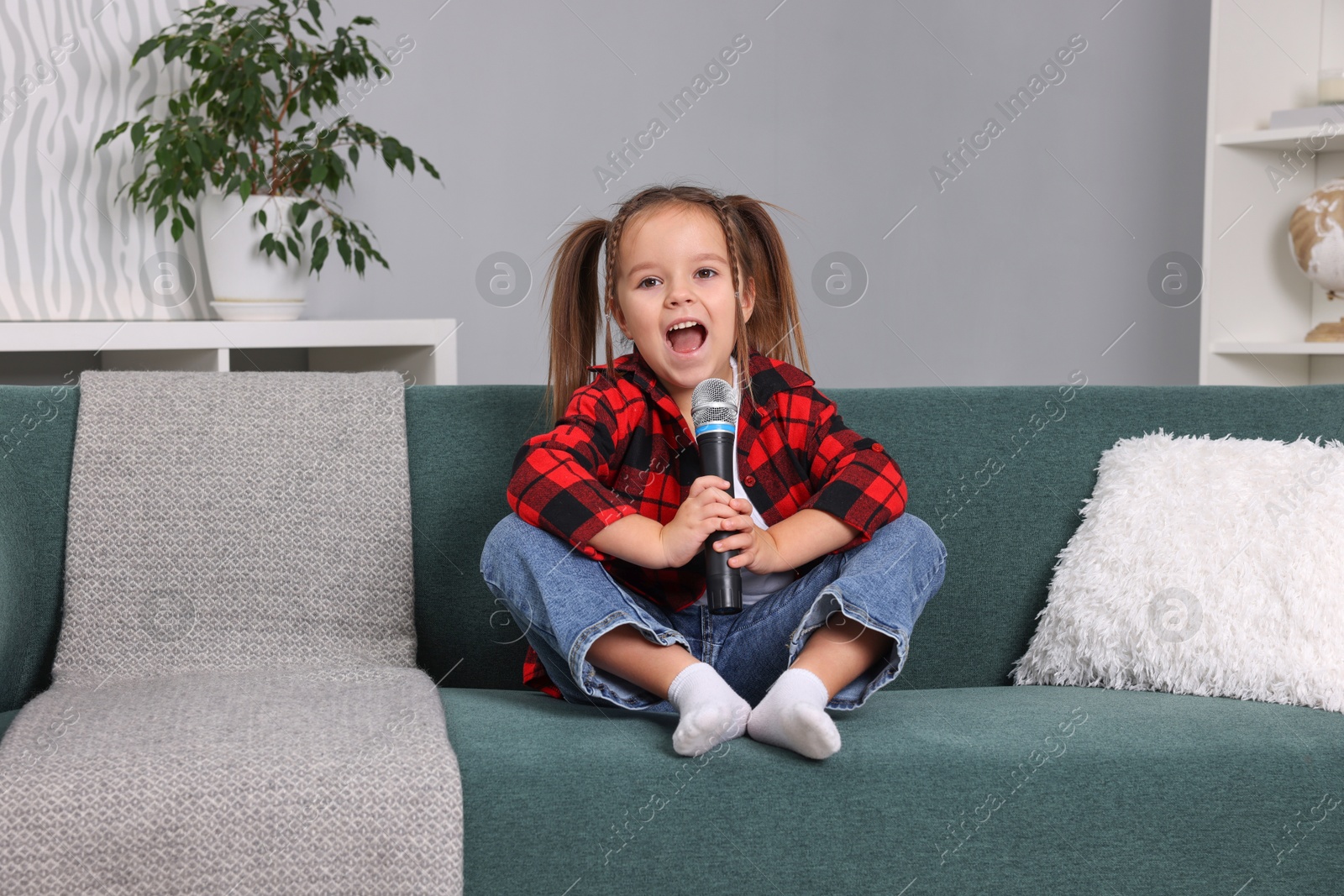 Photo of Cute girl with microphone singing on sofa at home