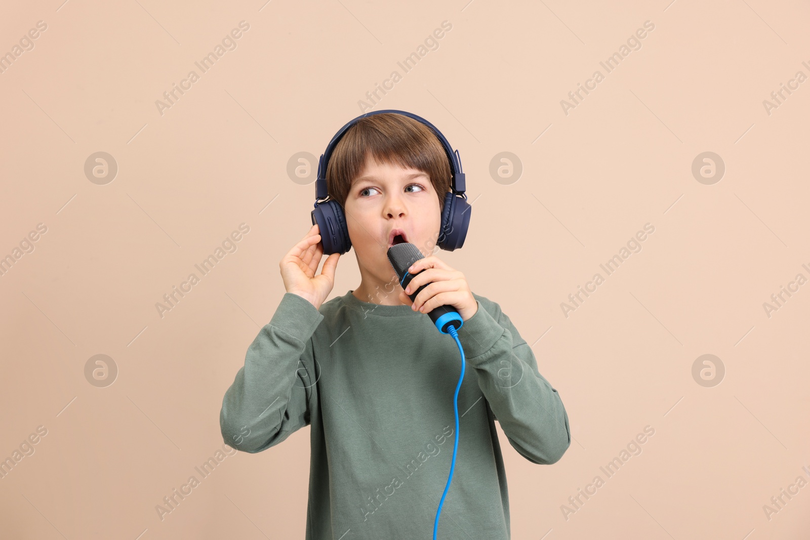 Photo of Cute boy with microphone in headphones singing near beige wall