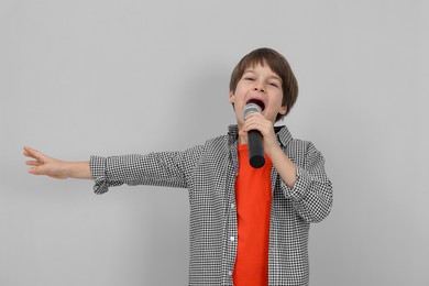 Photo of Cute boy with microphone singing near grey wall