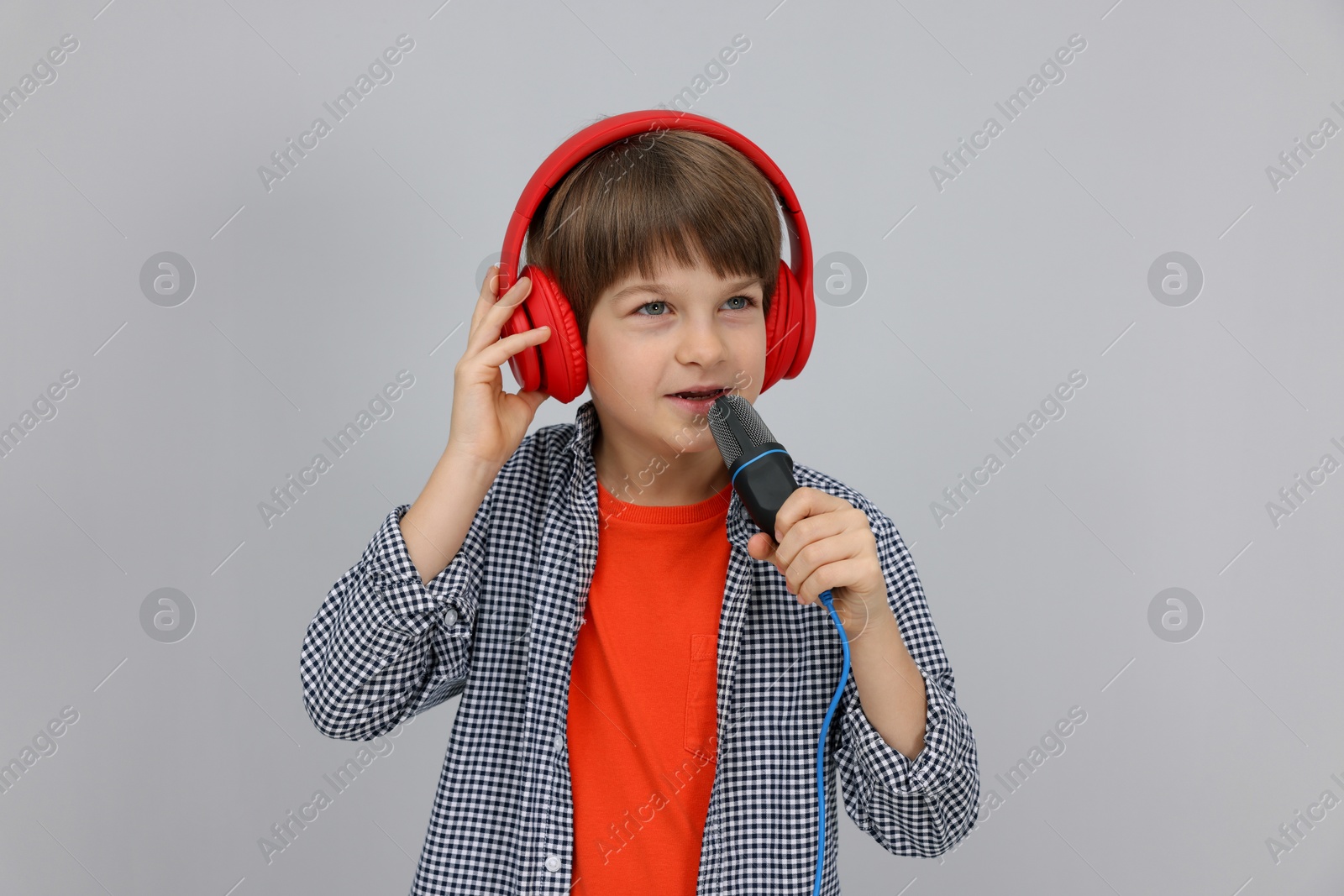 Photo of Cute boy with microphone in headphones singing near grey wall