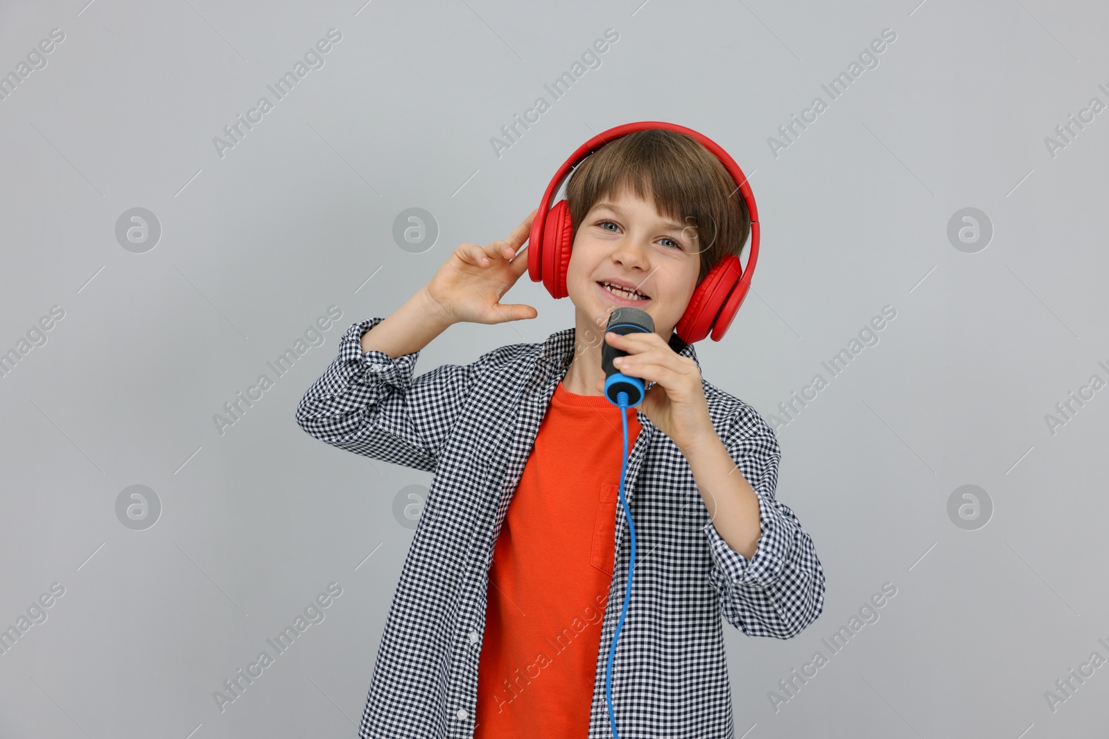 Photo of Cute boy with microphone in headphones singing near grey wall