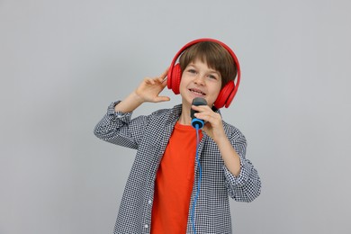 Photo of Cute boy with microphone in headphones singing near grey wall