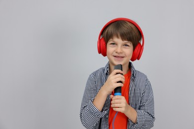 Photo of Cute boy with microphone in headphones singing near grey wall. Space for text