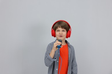 Photo of Cute boy with microphone in headphones singing near grey wall. Space for text