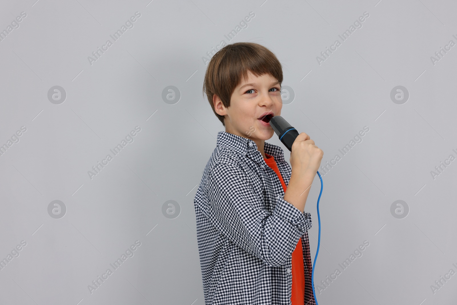 Photo of Cute boy with microphone singing near grey wall. Space for text