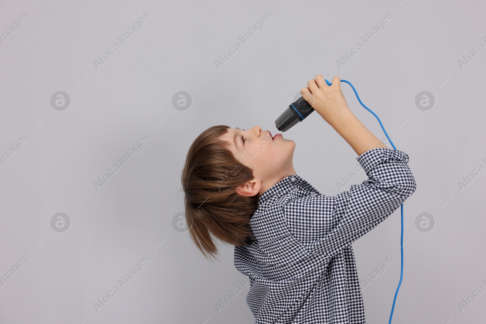 Photo of Cute boy with microphone singing near grey wall. Space for text