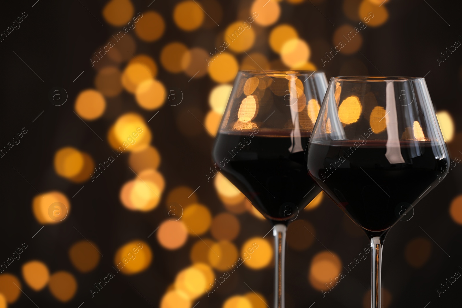 Photo of Tasty red wine in glasses against dark background with blurred lights, closeup. Bokeh effect