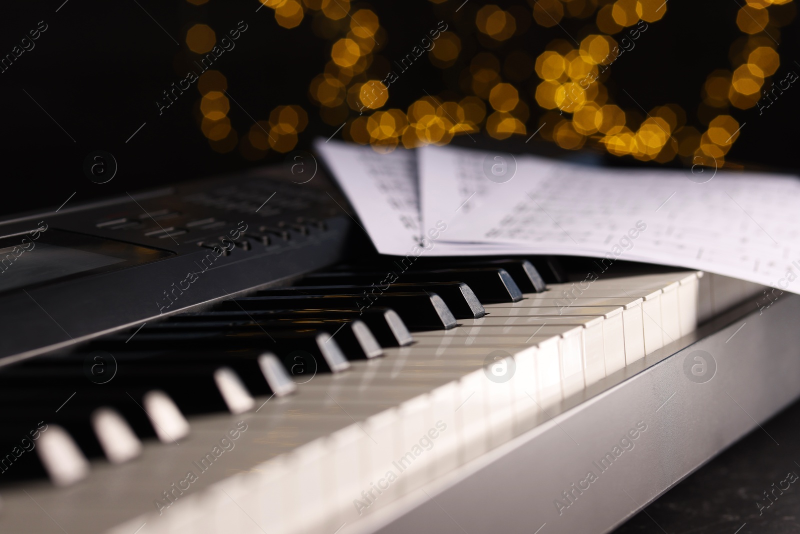 Photo of Sheets with musical notes on piano against blurred lights, closeup. Bokeh effect