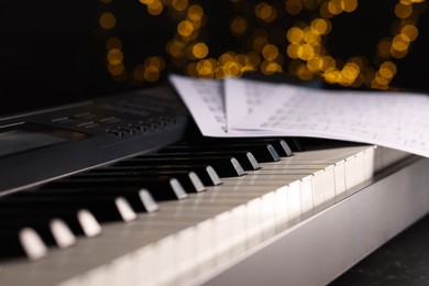 Photo of Sheets with musical notes on piano against blurred lights, closeup. Bokeh effect