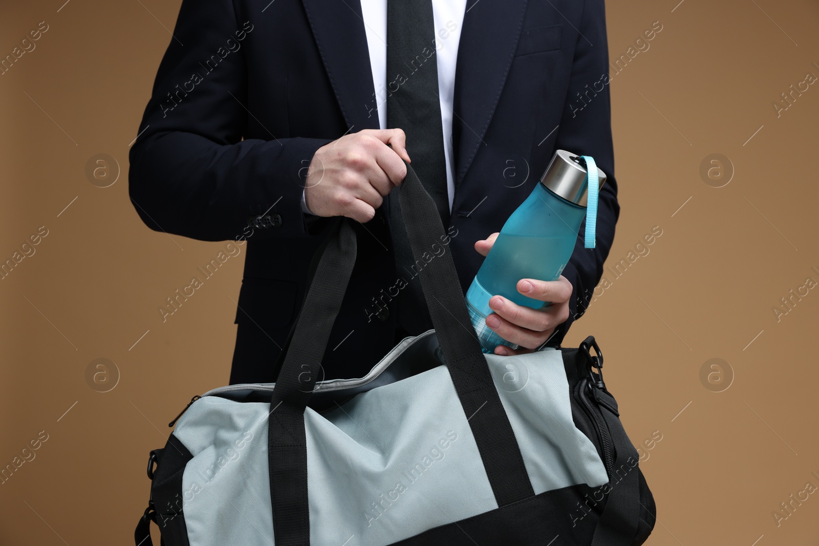 Photo of Man in suit putting bottle of water into gym bag on brown background, closeup