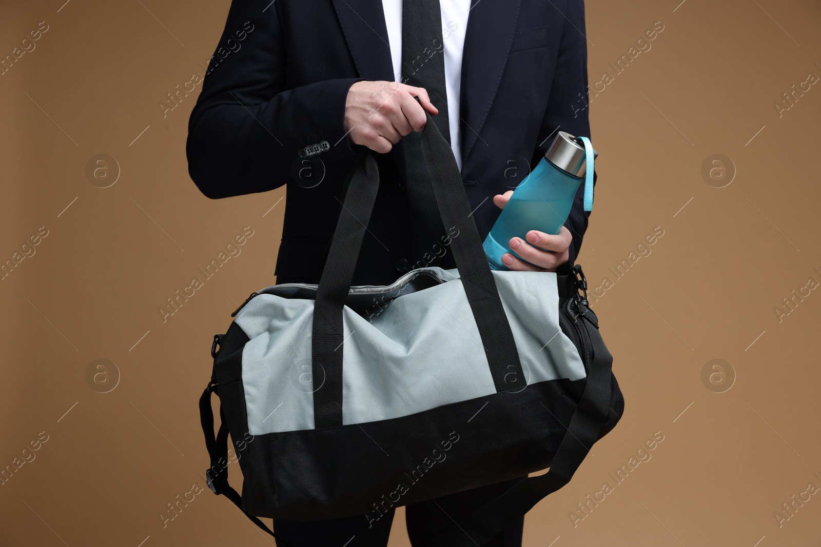 Photo of Man in suit putting bottle of water into gym bag on brown background, closeup