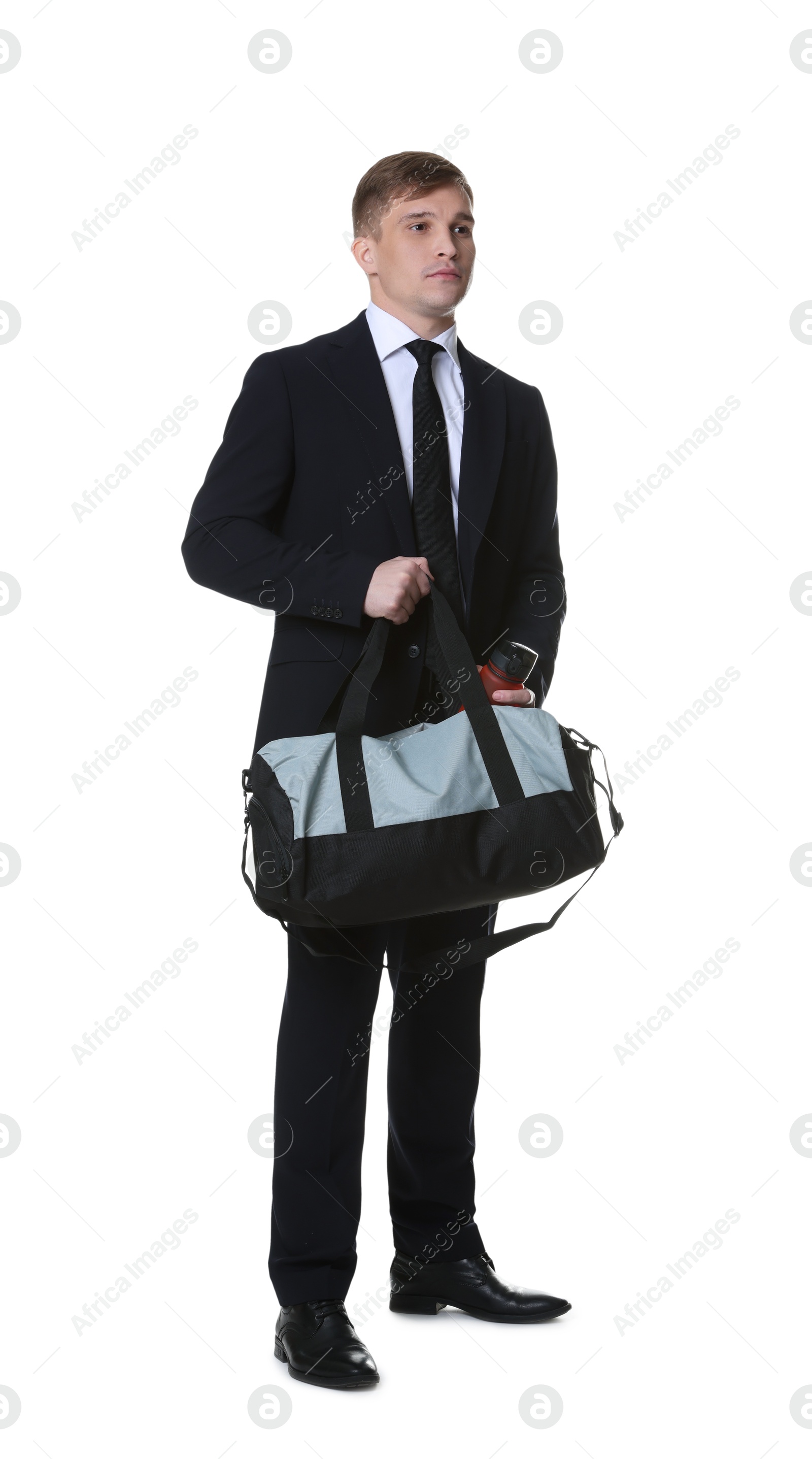 Photo of Young man in suit putting bottle of water into gym bag on white background