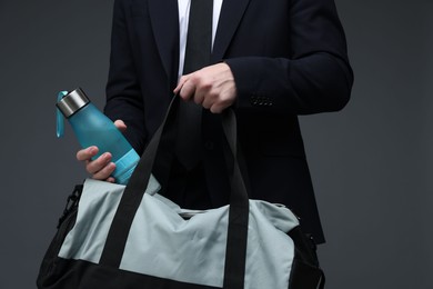 Photo of Man in suit putting bottle of water into gym bag on dark grey background, closeup