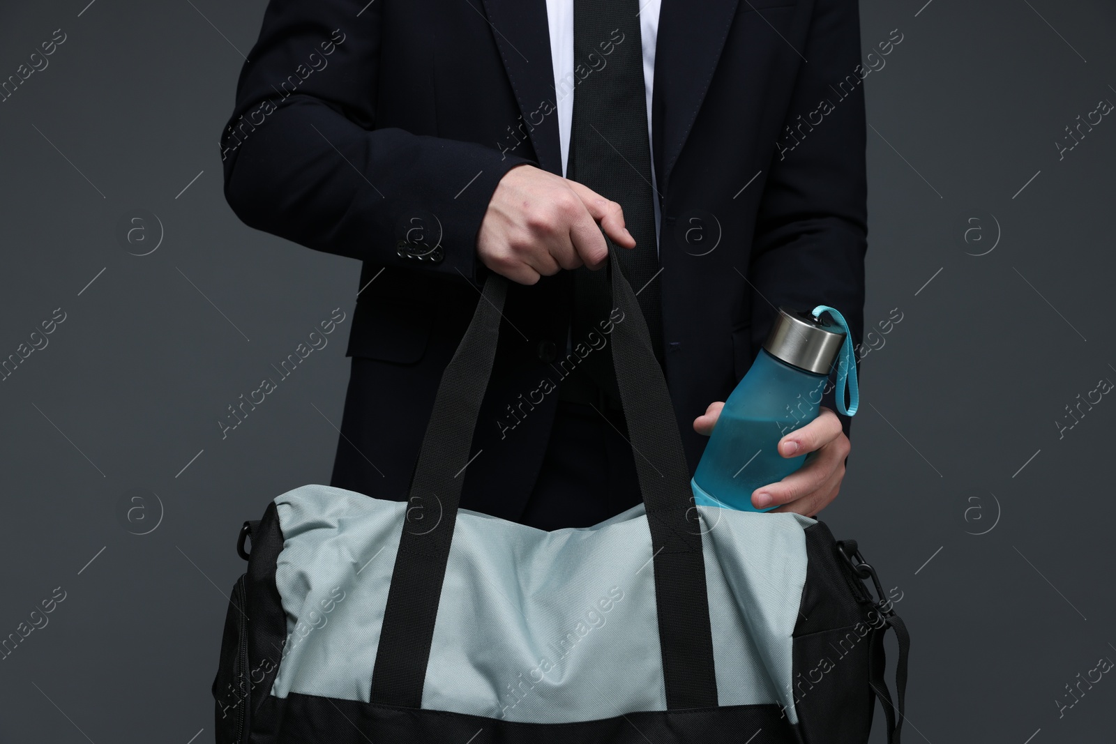 Photo of Man in suit putting bottle of water into gym bag on dark grey background, closeup