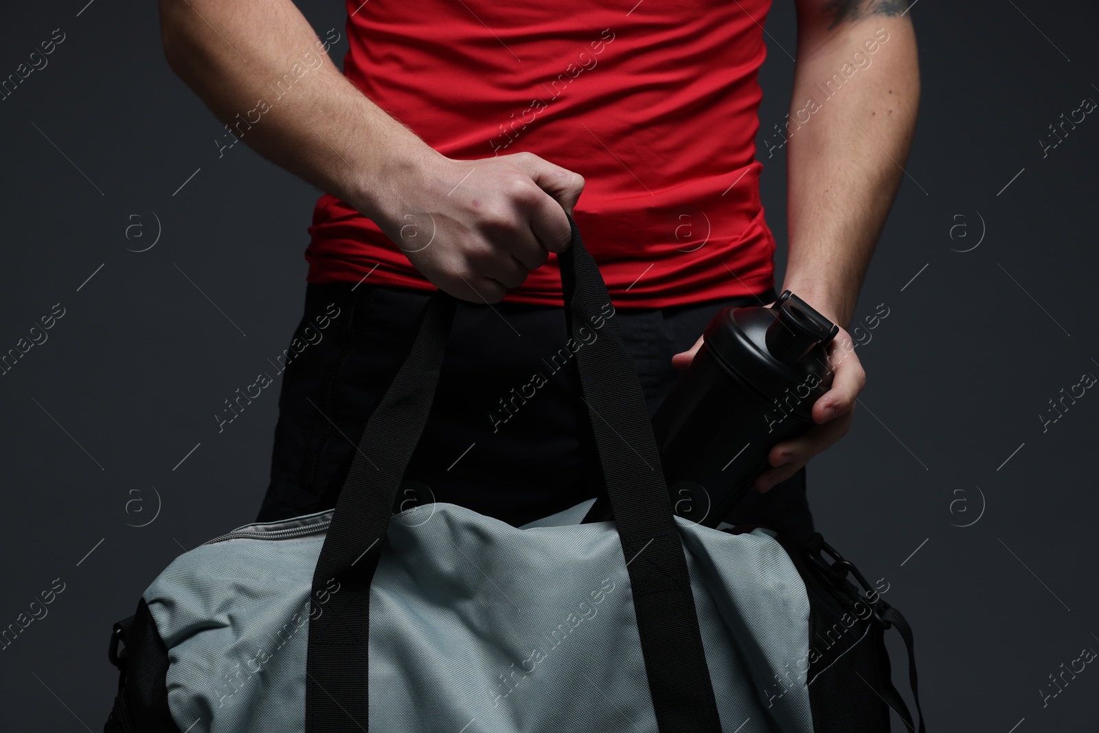 Photo of Man putting bottle of water into gym bag on dark grey background, closeup