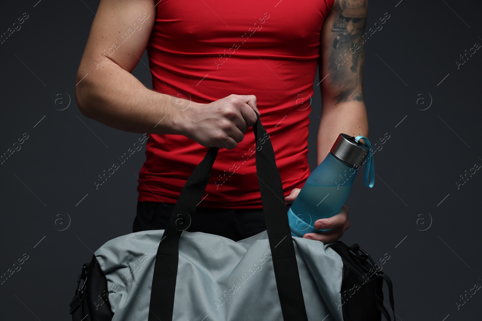 Photo of Man putting bottle of water into gym bag on dark grey background, closeup