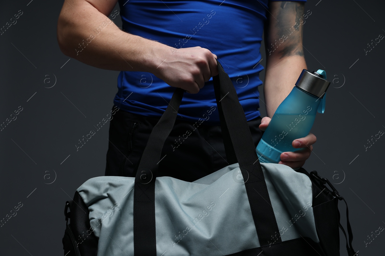 Photo of Man putting bottle of water into gym bag on dark grey background, closeup