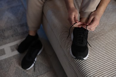 Photo of Man tying shoelace of sneaker at home, closeup